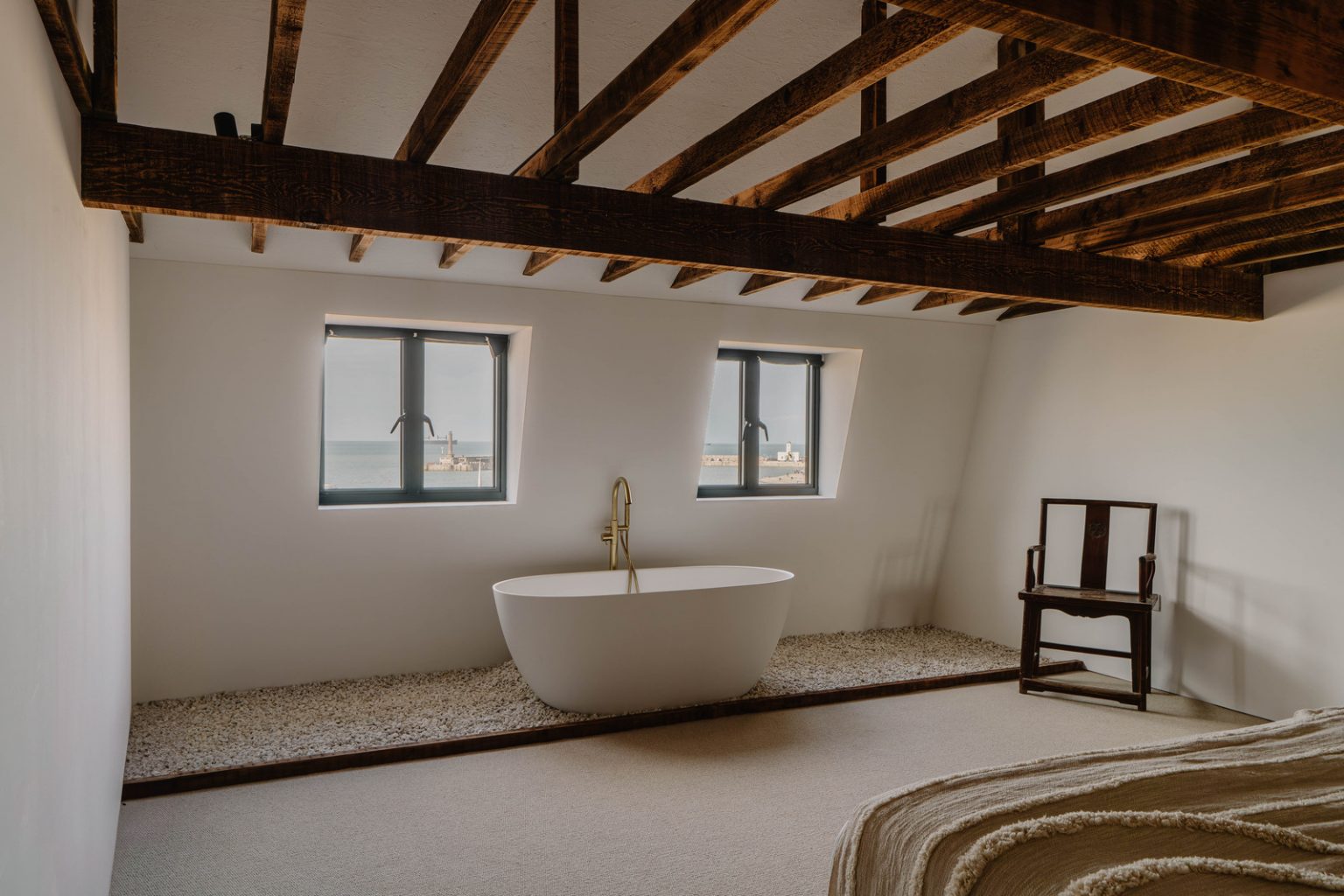 baignoire îlot design dans chambre avec poutres et mur de pierres décoration naturelle